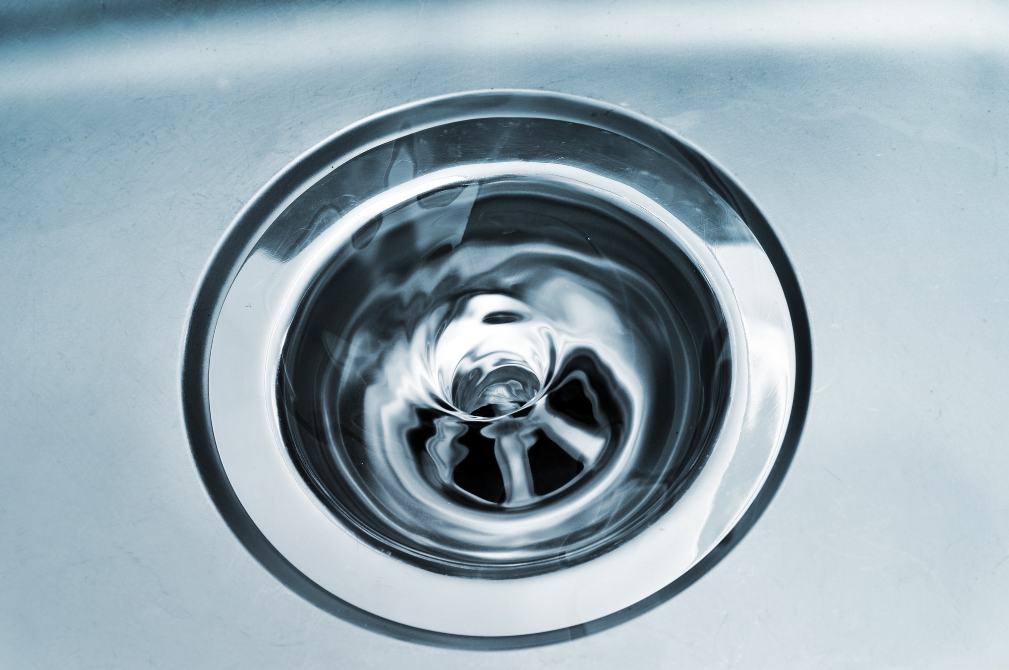 Swirling water in a stainless steel sink drain, showcasing the drain's circular design and the motion of liquid flowing down.