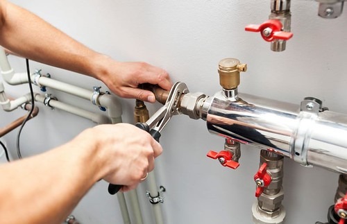 A technician uses a wrench to tighten a valve on a plumbing system, showcasing hands-on maintenance work in a mechanical setting.