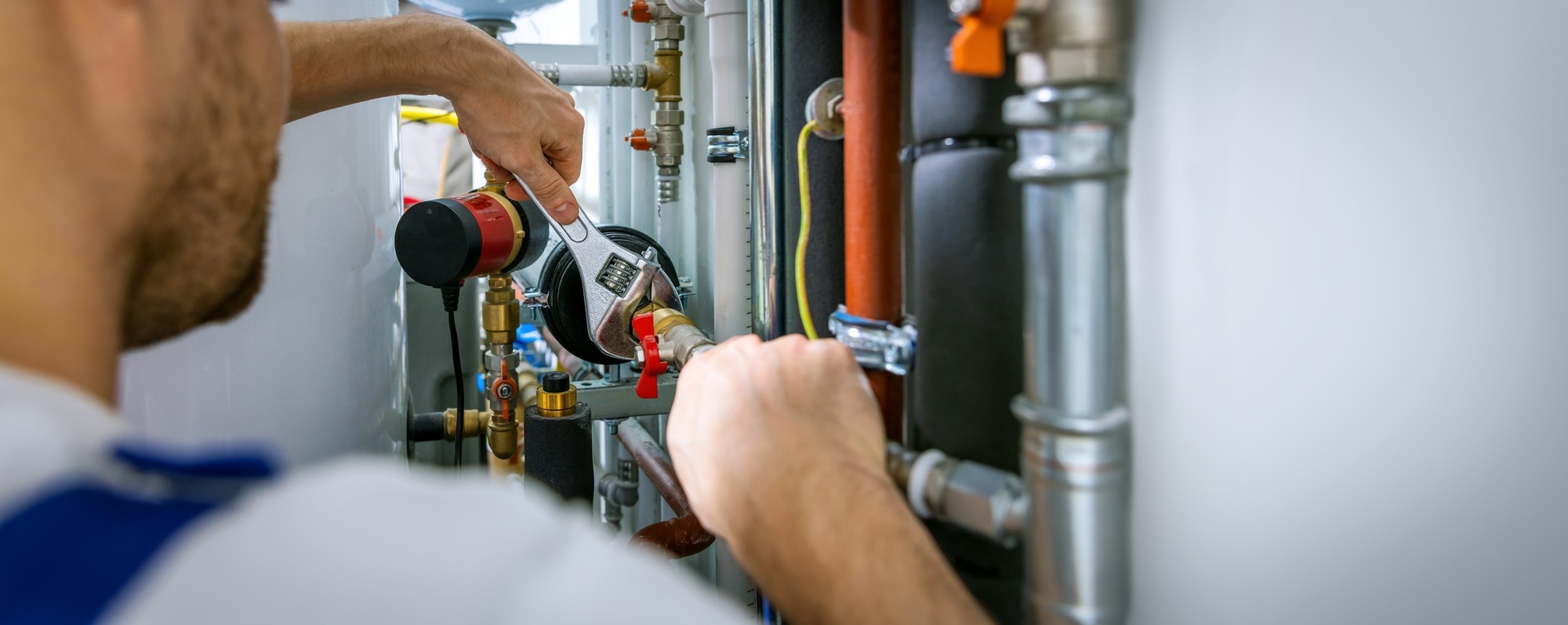 A technician adjusts plumbing fixtures with a wrench, showcasing work on pipes and valves in a maintenance setting. This highlights plumbing repair tasks.