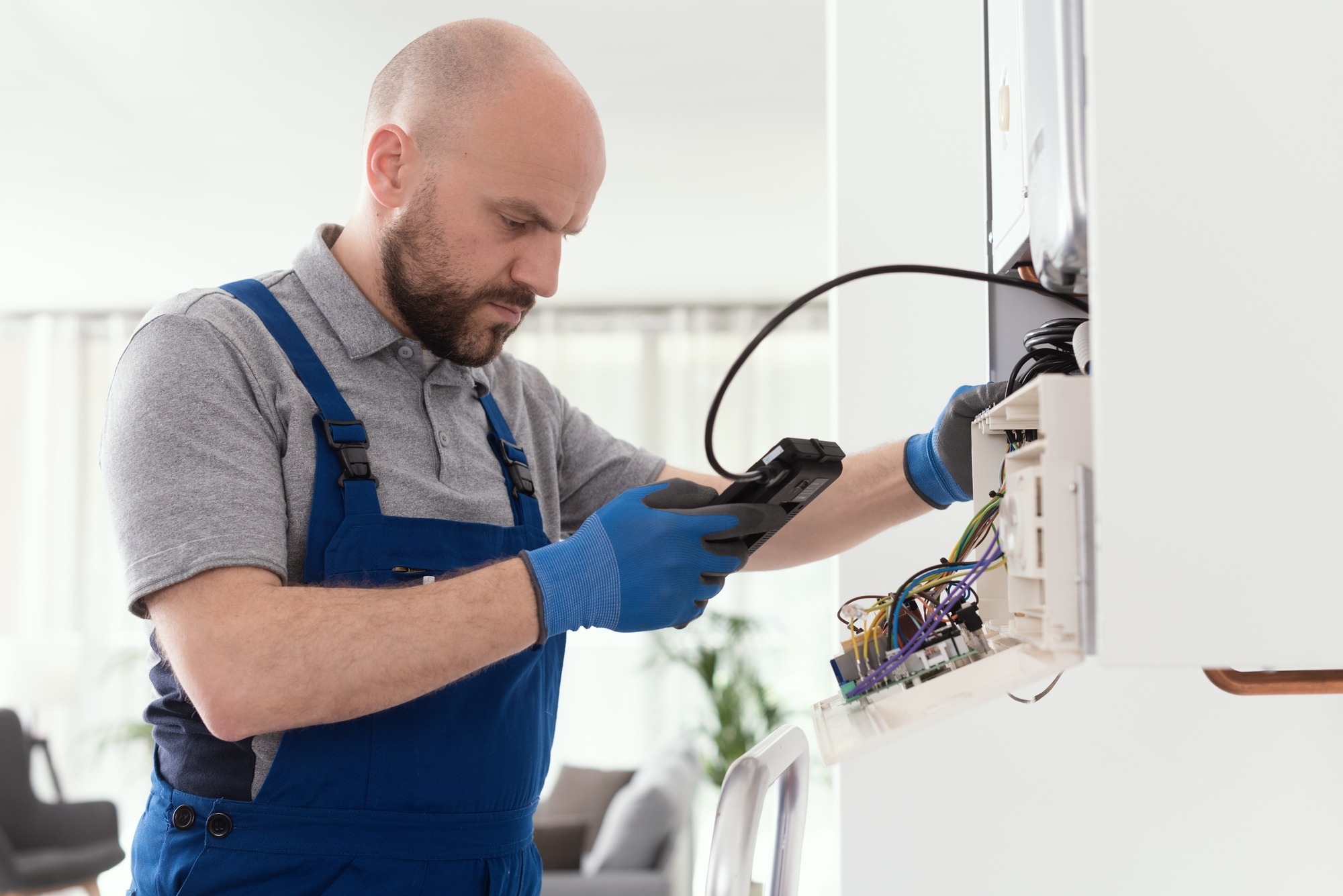 Technician wearing blue gloves inspects wiring and connections while testing equipment in a modern interior setting.