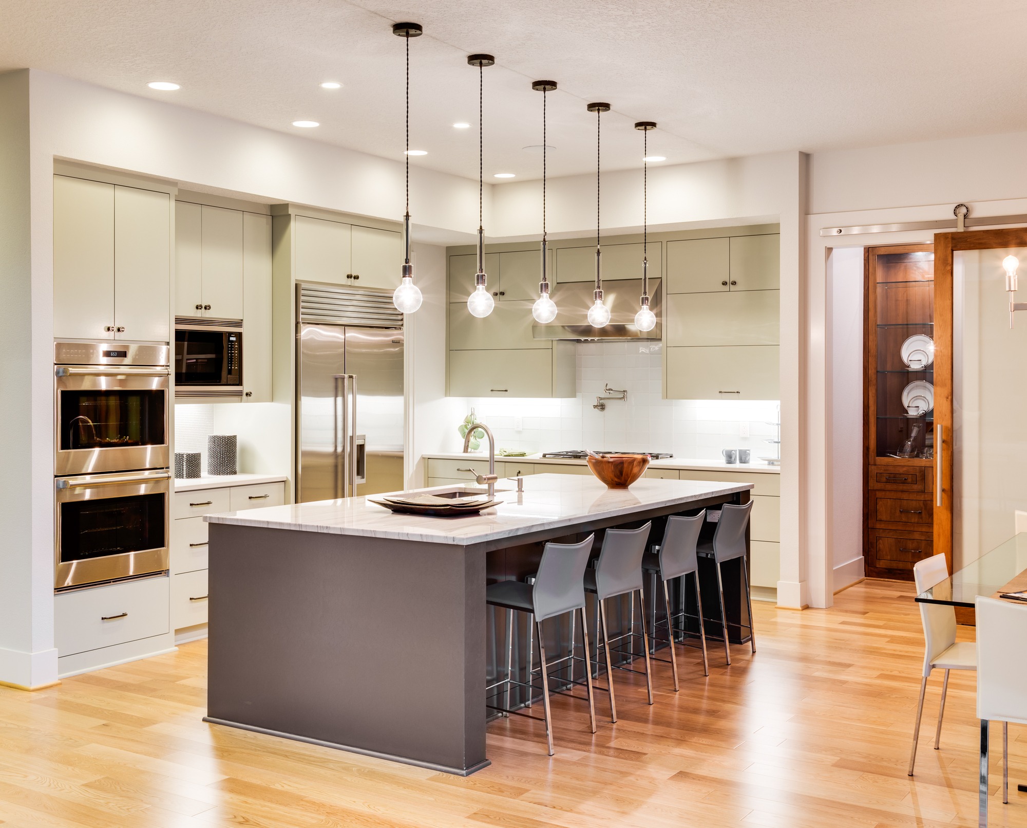 Modern kitchen featuring sleek cabinetry, stainless steel appliances, and a large island with seating. Stylish pendant lights enhance the bright atmosphere.