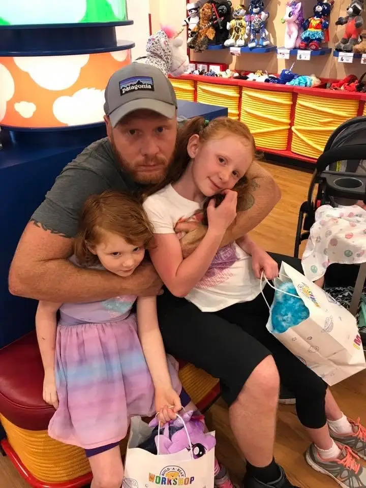 The owner of Around the Clog smiling with his two young daughters, each holding a Build-A-Bear Workshop gift bag.